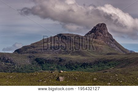 Assynt Peninsula Scotland - June 7 2012: Brown mountain peak and adjacent hill under heavy brownish skies fronted by green wild rough slopes east of Loch Buine Moire.