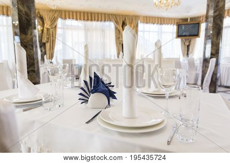 Festive table setting in classic style in a white restaurant interior, setout, layout. holiday table decor concept. Expectation of guests.