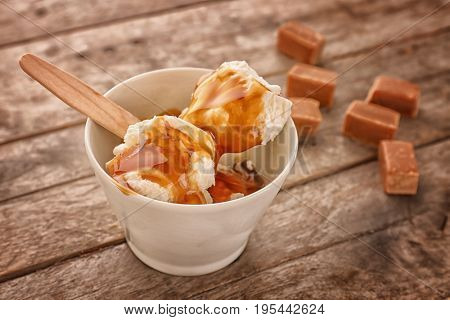 Bowl with vanilla ice cream and caramel sauce on table