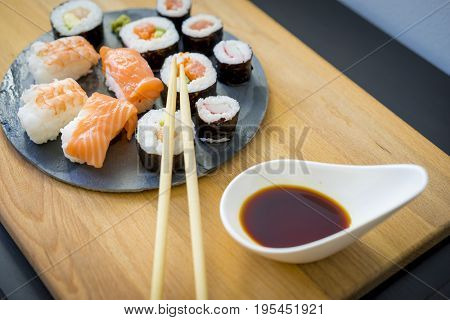 Maki on a wooden table on black slate plate with soy sauce and chopsticks