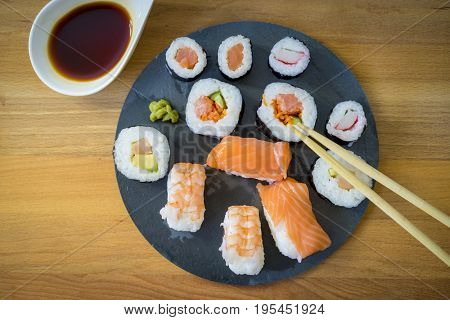 Sushi on a wooden table on black slate plate with soy sauce and chopsticks