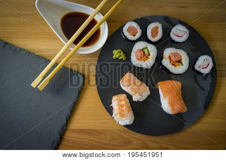 Sushi on a wooden table on black slate plate with soy sauce and chopsticks