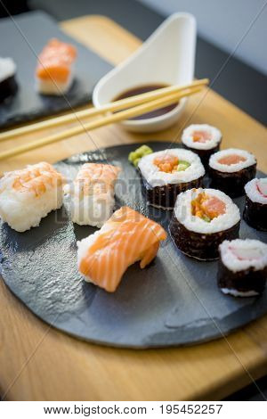 Sushi on a wooden table on black slate plate with soy sauce and chopsticks