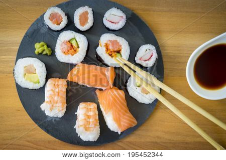 Sushi on a wooden table on black slate plate with soy sauce and chopsticks