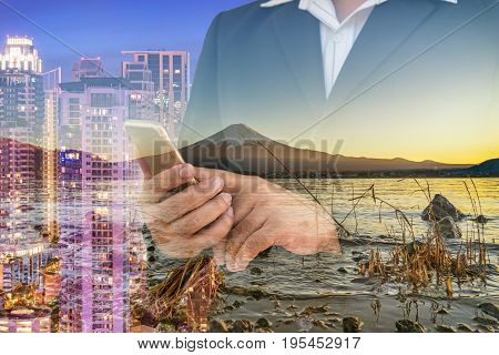 double exposure of business man check his smartphone mountain fuji and cityscape