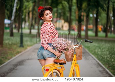 Pinup girl on retro bicycle with backet of flowers