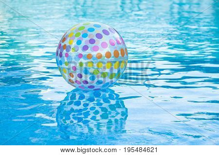 holiday lifestyle, rest and summer swimming concept - on surface of blue pool water is inflatable transparent ball decorated by multi-colored circles, entertainment in hotel or backyard of household