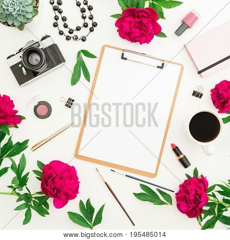Beauty blogger or freelancer desk workspace with clipboard, notebook, retro camera, red flowers, coffee mug and accessories on white background. Flat lay, top view.