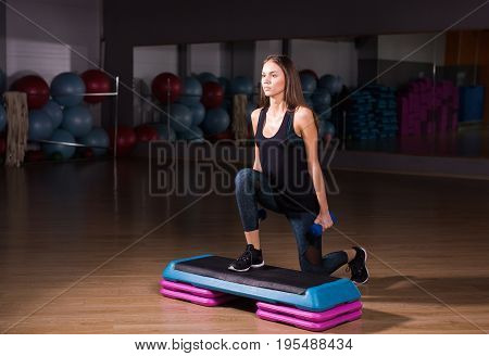 fitness, sport, training, gym and lifestyle concept - woman stepping with dumbbells on step platform in gym.