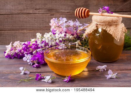 Jar of honey with wildflowers on a dark wooden background.