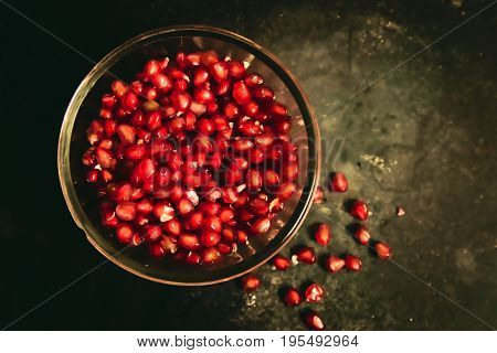 Fresh, peeled and juicy pomegranate seeds in glass bowl on a dark background.