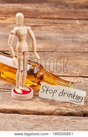 Stop drinking and become thinking. Human wooden dummy, alcohol beverage in glass bottle, message, wooden background.