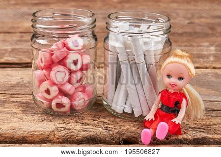 Candies, cigarettes, doll, glass jars. Metaphor concept of cigarette addiction. Do not smoke, buy your child sweets.