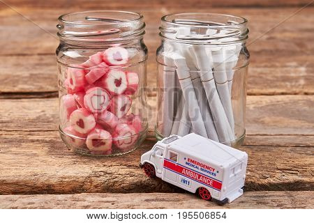 Jars with sweets and cigarettes, ambulance. Unhealthy lifestyle leads to illness.