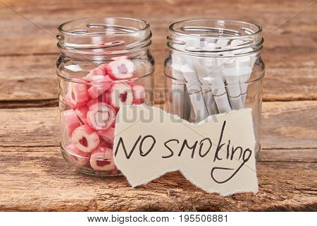 No smoking concept. Glass jars with candies and tobacco cigarettes, paper massage, wooden background.