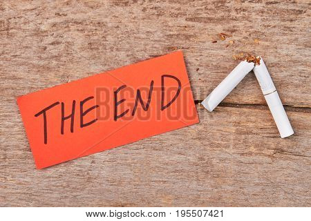 Message the end, broken cigarette. White broken tobacco cigarette on wooden background, top view.