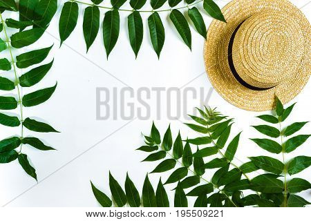 Green leaf branches and straw haton white background. flat lay, top view. Copy space. Still life