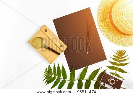 Straw hat with green leaves and old camera on white background, Summer background. Top view. Copy space. Still life. Flat lay. Sun flare