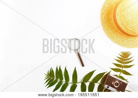 Straw hat with green leaves and old camera on white background, Summer background. Top view. Copy space. Still life. Flat lay. Sun flare