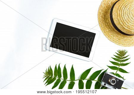 Straw hat with green leaves, tablet and old camera on white background, Summer background. Top view. Copy space. Still life. Flat lay