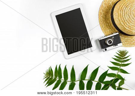 Straw hat with green leaves, tablet and old camera on white background, Summer background. Top view. Copy space. Still life. Flat lay