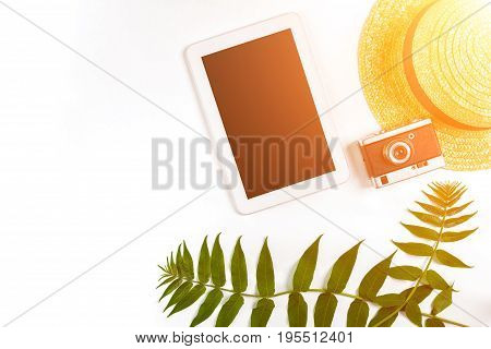 Straw hat with green leaves, tablet and old camera on white background, Summer background. Top view. Copy space. Still life. Flat lay. Sun flare