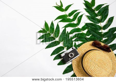 Straw hat with green leaves and old camera on white background, Summer background. Top view. Copy space. Still life. Flat lay