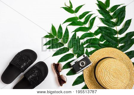 Straw hat with green leaves and old camera on white background, Summer background. Top view. Copy space. Still life. Flat lay