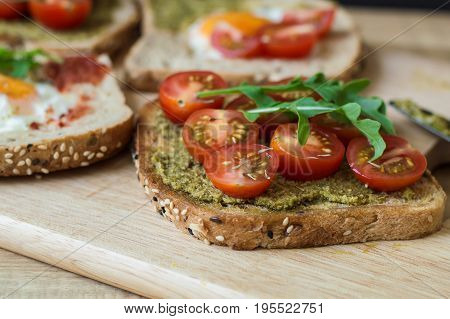 Breakfast toasts with vegetables. Sandwich with multi cereal bread pesto sauce red cherry tomato arugula on wooden board. Healthy eating