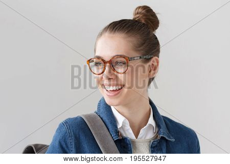Indoor Closeup Of Nice Teenager Girl Wearing Big Trendy Spectacles And Denim Jacket Isolated On Gray