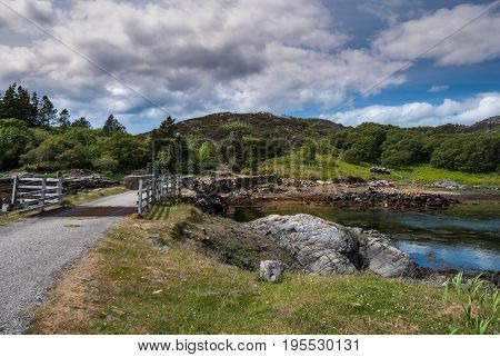 Assynt Peninsula Scotland - June 7 2012: Short stone bridge with cattle grill over creek landing into Atlantic Ocean inlet South of Loch An Arbhair under heavy sky. Forested hills and ocean waters.