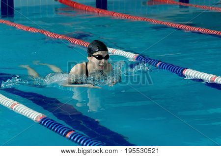 Young Woman In Goggles And Cap Swimming Breaststroke Stroke Style In The Blue Water Indoor Race Pool