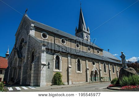 Church and sculpture in the village of Thorens-Glières, with blue and sunny sky. Located in the department of Haute-Savoie, Auvergne-Rhône-Alpes region, in south-eastern France