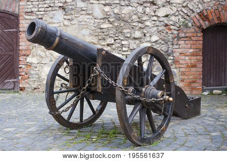 Ancient cannon on wheels in castle with brick wall background.