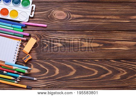 Border from stationery - pencils pen note erazer paint on wooden background. Back to school. Top view. Place for text.