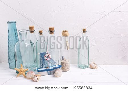 Ocean or sea theme home decorations. Decorative bottles wooden boat starfish shells on white textured background. Selective focus.