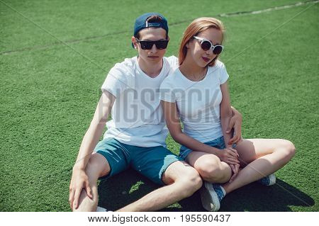 Young couple with in white T-shirts are sitting on the lawn. Mock up.
