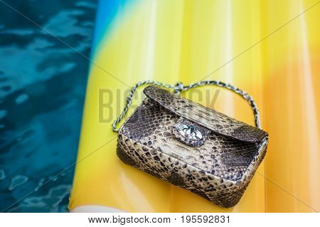 Fashion luxury snakeskin python handbag on a Inflatable Yellow Mattress in Swimming Pool.