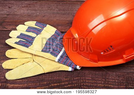 Orange hard hat and gloves for work on wood background