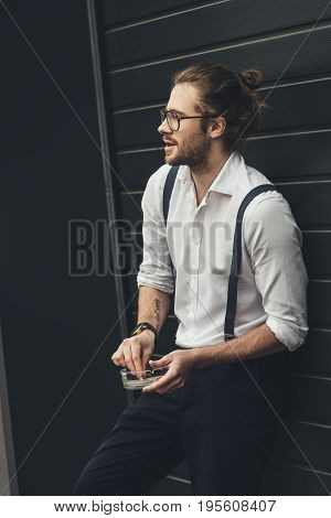 Handsome Stylish Young Man In Spectacles Holding Ashtray While Smoking And Looking Away
