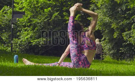Young woman doing yoga exercises in the park. Akarna Dhanurasana