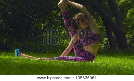 Young woman doing yoga exercises in the park. Akarna Dhanurasana