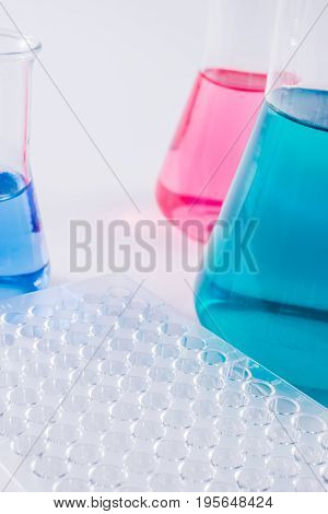 research, science and clinic background. 96 well micro plate and  laboratory beakers with colorful liquids and reagents.