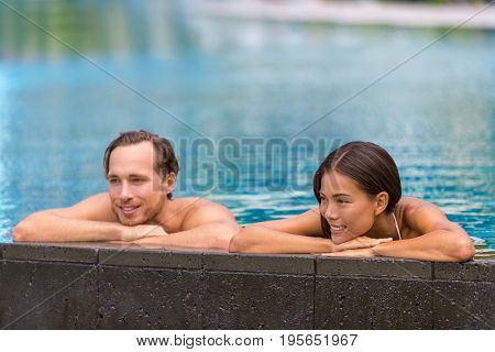 Swimming pool wellness resort couple relaxing sunbathing in infinity luxury retreat pool in hotel. Tropical travel destination getaway.