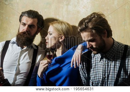 Group of friends relaxing with alcoholic drinks. Girl with glass of liqueur and men with wine bottle on beige wall. Friendship and convives. Alcohol and appetizer. Unhealthy lifestyle and bad habits