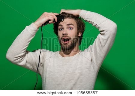 surprised man shaving with electric razor or shaver trimmer with long hair and beard on face in white underwear on green background morning and everyday life barbershop and fashion
