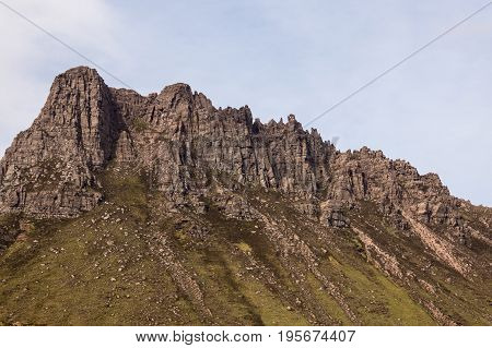 Assynt Peninsula Scotland - June 7 2012: Closeup of brown Mountain ridge along Loch Lurgainn under white sky. Green vegetation on foothills.
