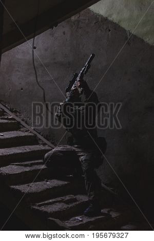 Strikeball player with weapons on stairs in entrance of destroyed house