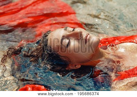 beautiful young woman in red dress laying dowm in water