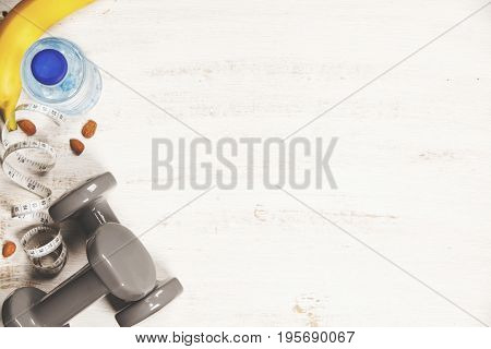 Fitness concept with dumbbells, water, measuring tape and fresh fruits on white wooden background